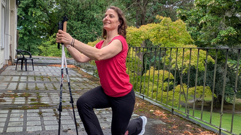 Therapeutin führt Übung mithilfe von Nordic Walking Stöcken aus